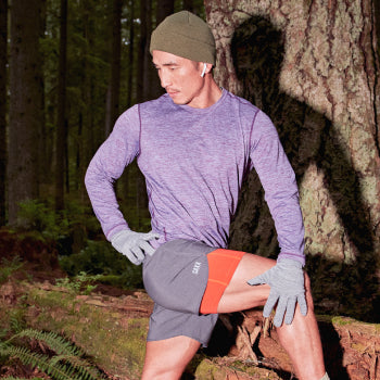 Man stretching on a running trail while wearing a purple long sleeve tee and gray running shorts