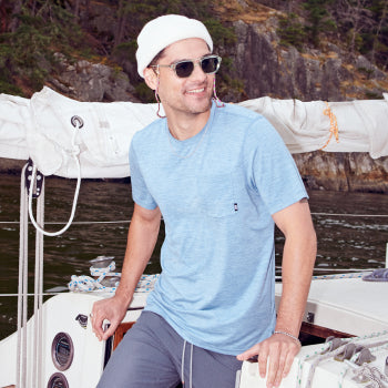 Man in blue shirt and sweat pants standing on boat in toque and sunglasses