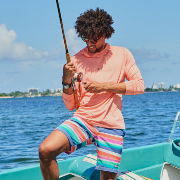 Man on boat in pink hoodie and striped board shirts with fishing pole