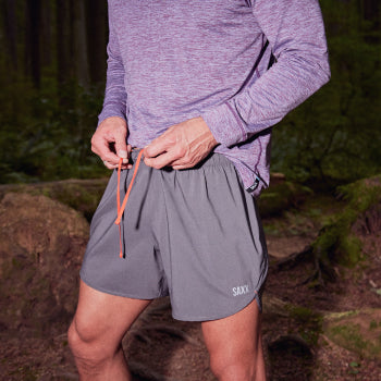 Man on a running trail wearing a purple long sleeve tee and gray running shorts