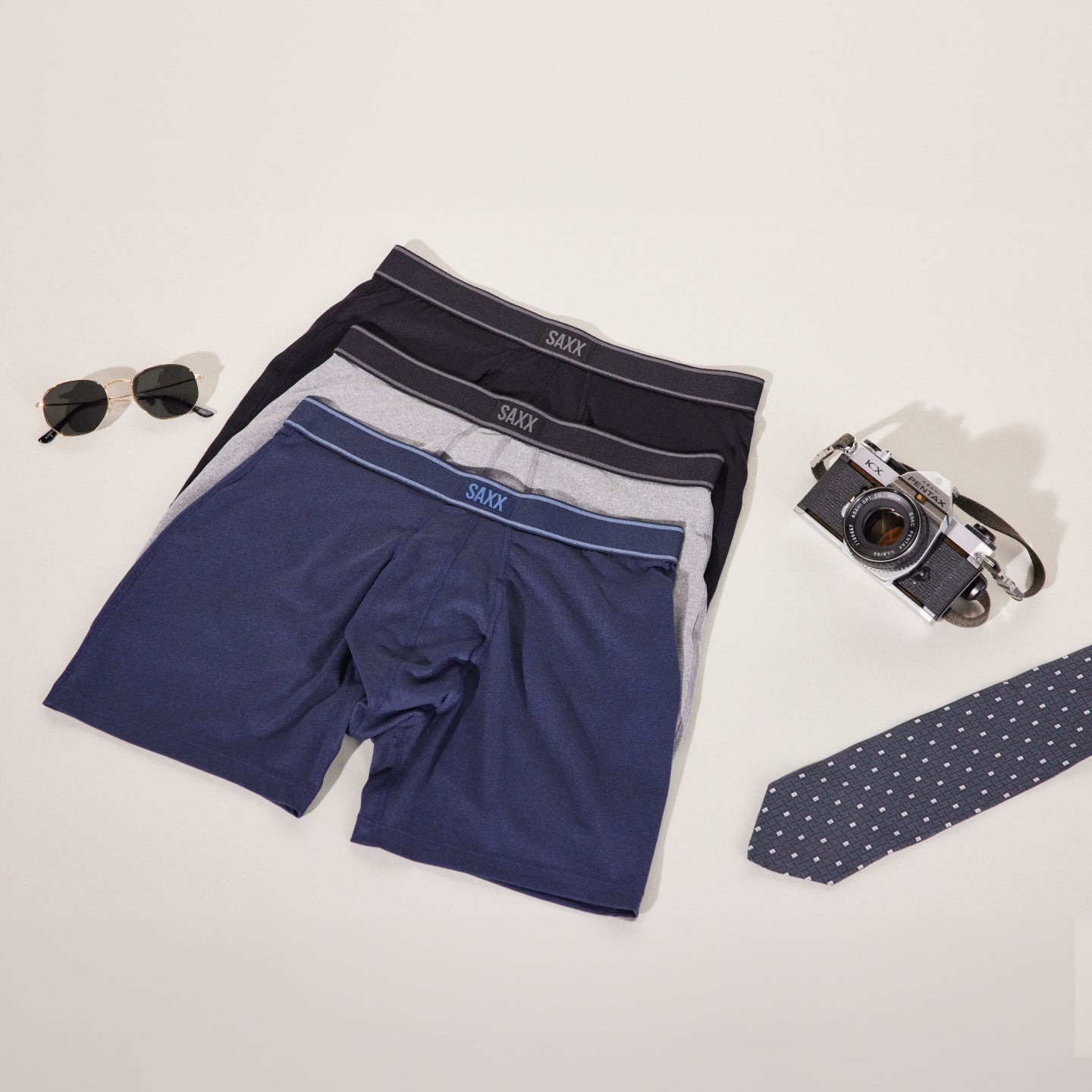 Three pairs of underwear resting beside sunglasses, camera, and necktie