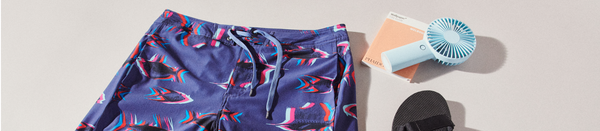 Blue patterned board shorts resting by hand fan and flip flops