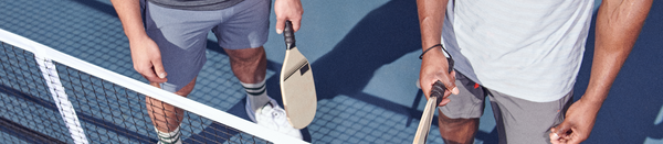 Two men in sport gear holding paddles on pickleball court