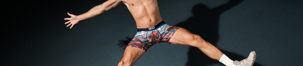 Shirtless man in patterned underwear and shoes jumping with arms spread out