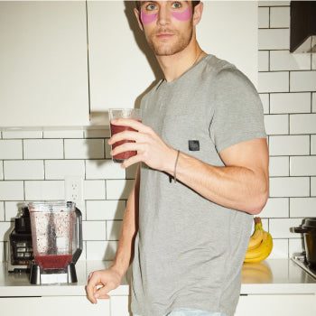 Man wearing grey shirt holding a glass of juice standing in kitchen