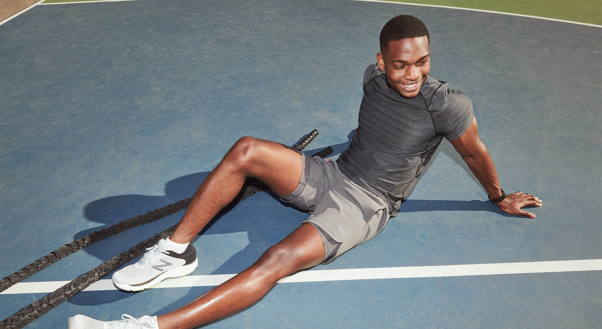 A person relaxing after a workout on a sports court wearing SAXX 2N1 shorts and SAXX Hot Shot Top