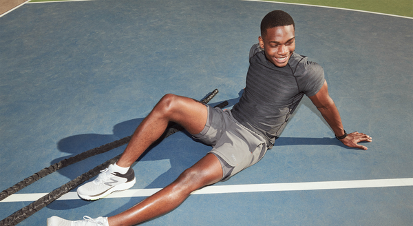 A person relaxing after a workout on a sports court wearing SAXX 2N1 shorts and SAXX Hot Shot Top