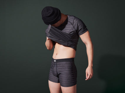 A person wearing DropTemp Cooling Mesh Boxer Briefs and Short Sleeve Crew, wiping sweat from their face
