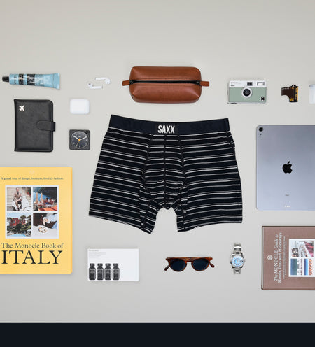 Dark striped boxer brief surrounded by travel essentials such as sunglasses and shaving kit