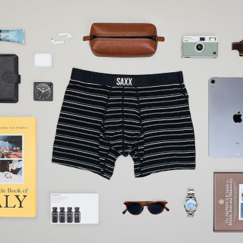 Dark striped boxer brief surrounded by travel essentials such as sunglasses and shaving kit