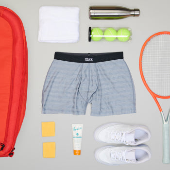 Grey boxer brief surrounded by tennis equipment such as racket balls and bag