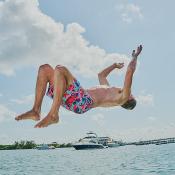 Shirtless man in floral swim shorts in mid air doing back flip