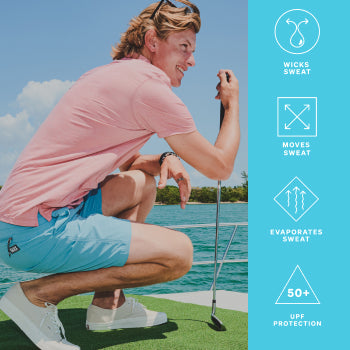 Man in pink polo shirt and blue shorts crouching on boat with golf club 