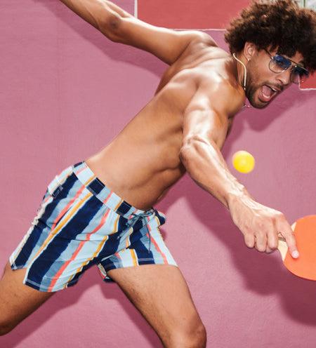 Shirtless man in striped swim shorts and sun glasses swinging ping pong racket