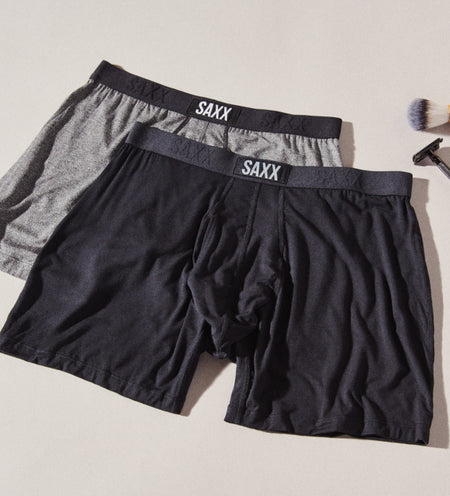 Two pairs of Boxer Briefs in blue and black lying next to a shaving razor and brush