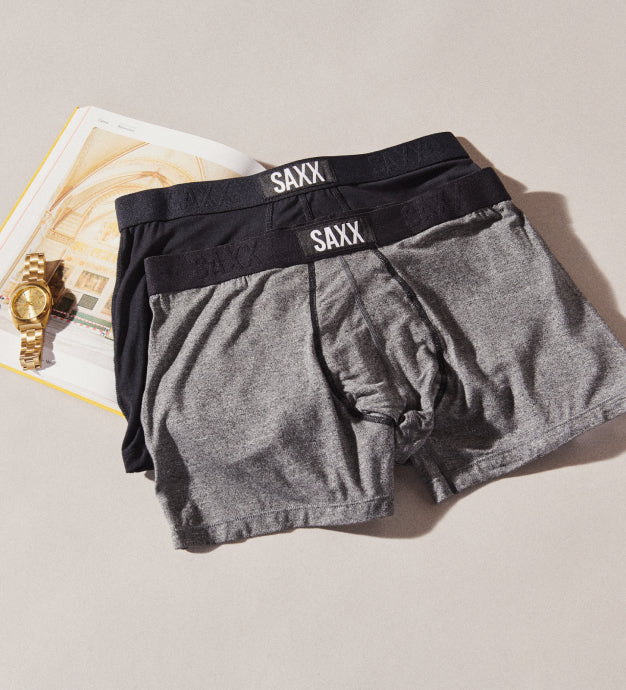 Two pairs of Trunks in gray and black lying next to a book and gold watch