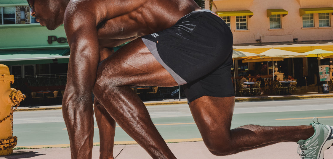 Shirtless man in black athletic shorts and shoes in starting position on city street