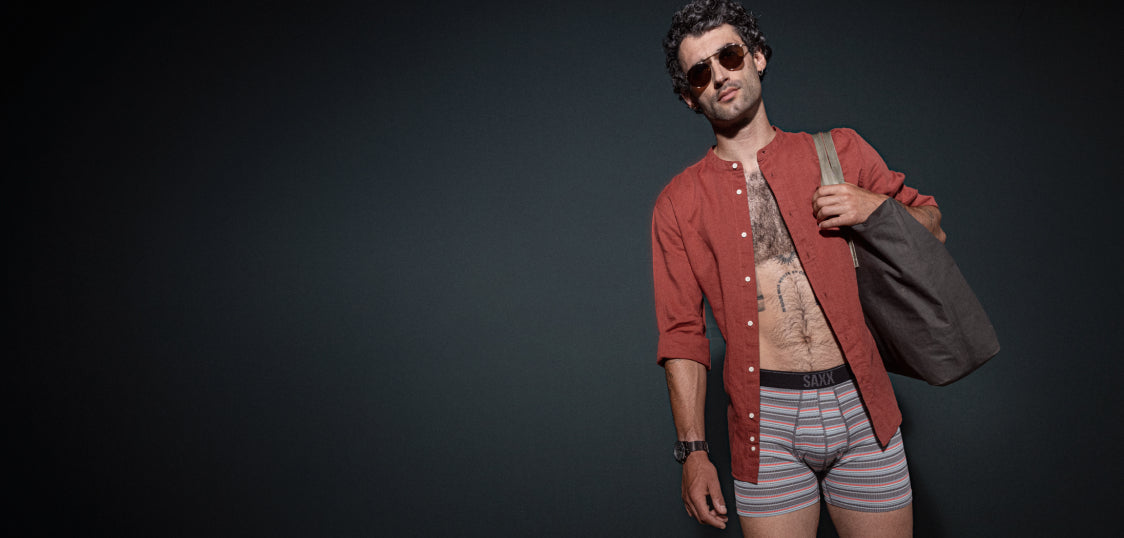 Tattooed man in underwear and unbuttoned shirt standing with tote bag on shoulder