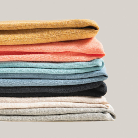 A neatly folded stack of different colored SAXX shirts on a neutral background.