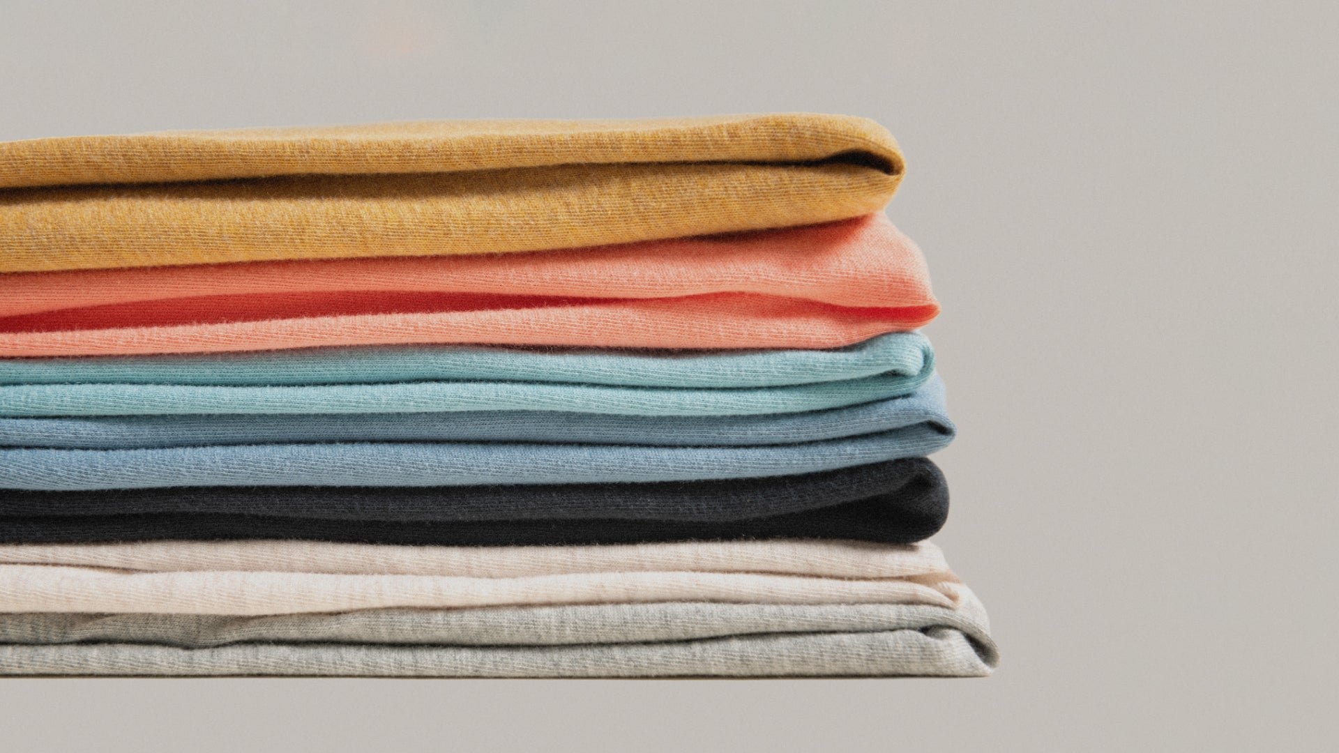 A neatly folded stack of different colored SAXX shirts on a neutral background.