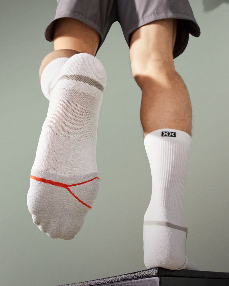 A person's feet wearing socks. Seen from the rear, one foot is raised to reveal the sole of the sock.