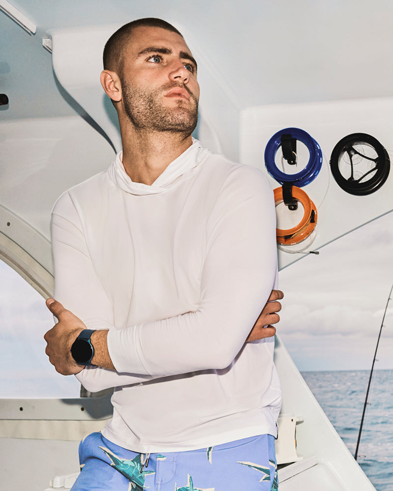 A man on a boat wearing a white hoodie. He has long eyelashes and is looking upwards.
