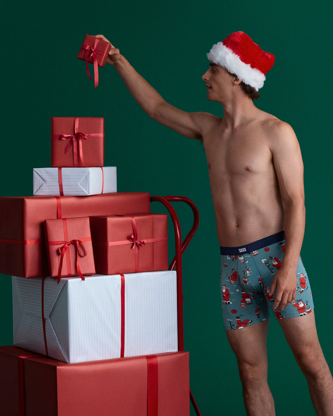 Man in Santa hat and underwear with Christmas presents on a green background