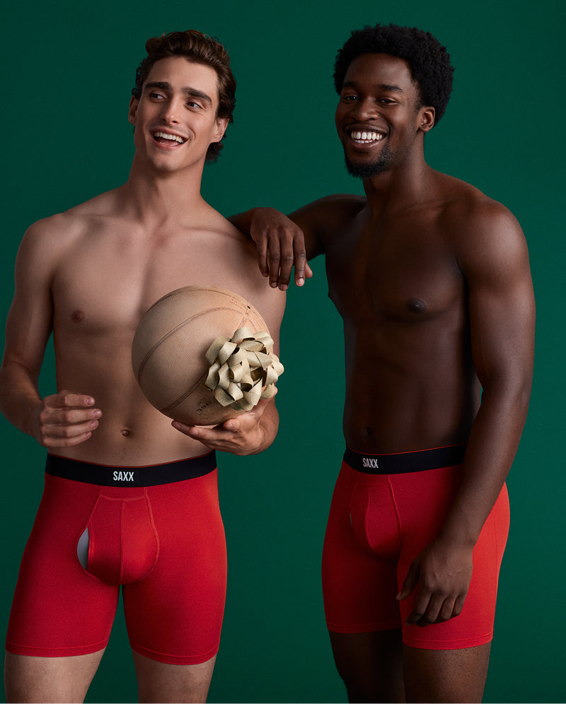 Two men in red SAXX boxer briefs holding a basketball with a gift bow on it