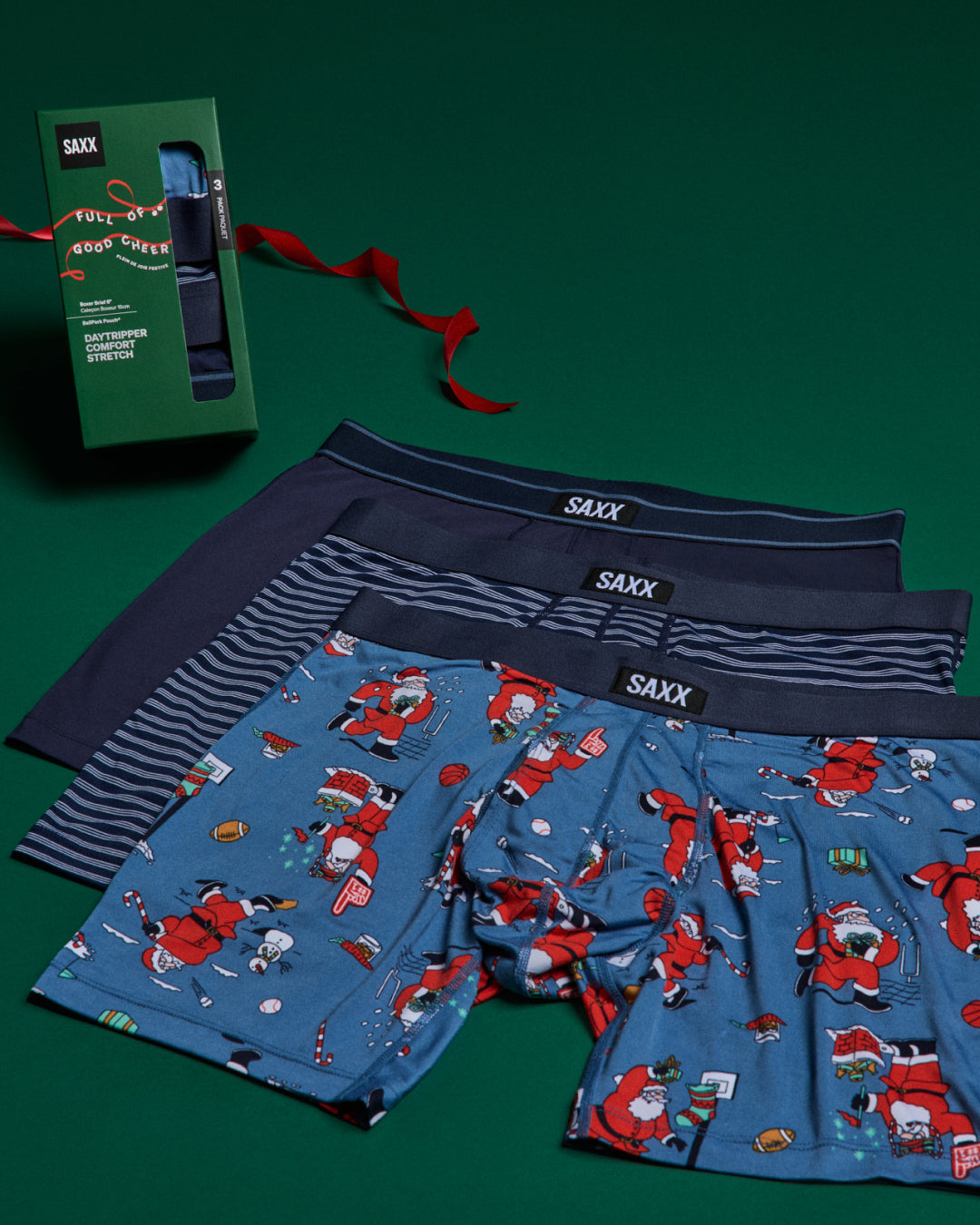 Three pairs of underwear stacked on top of each other next to a gift box against a green back drop.