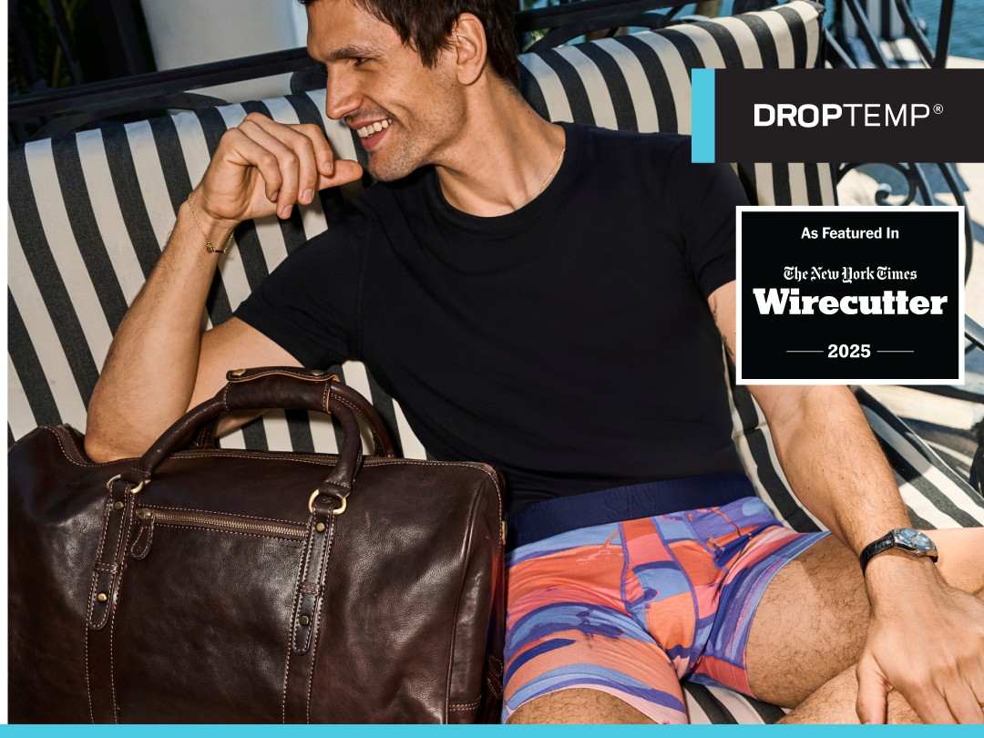 Man sitting on a striped couch with a leather bag, wearing a black shirt and colorful shorts, with 'DROPTEMP' branding.