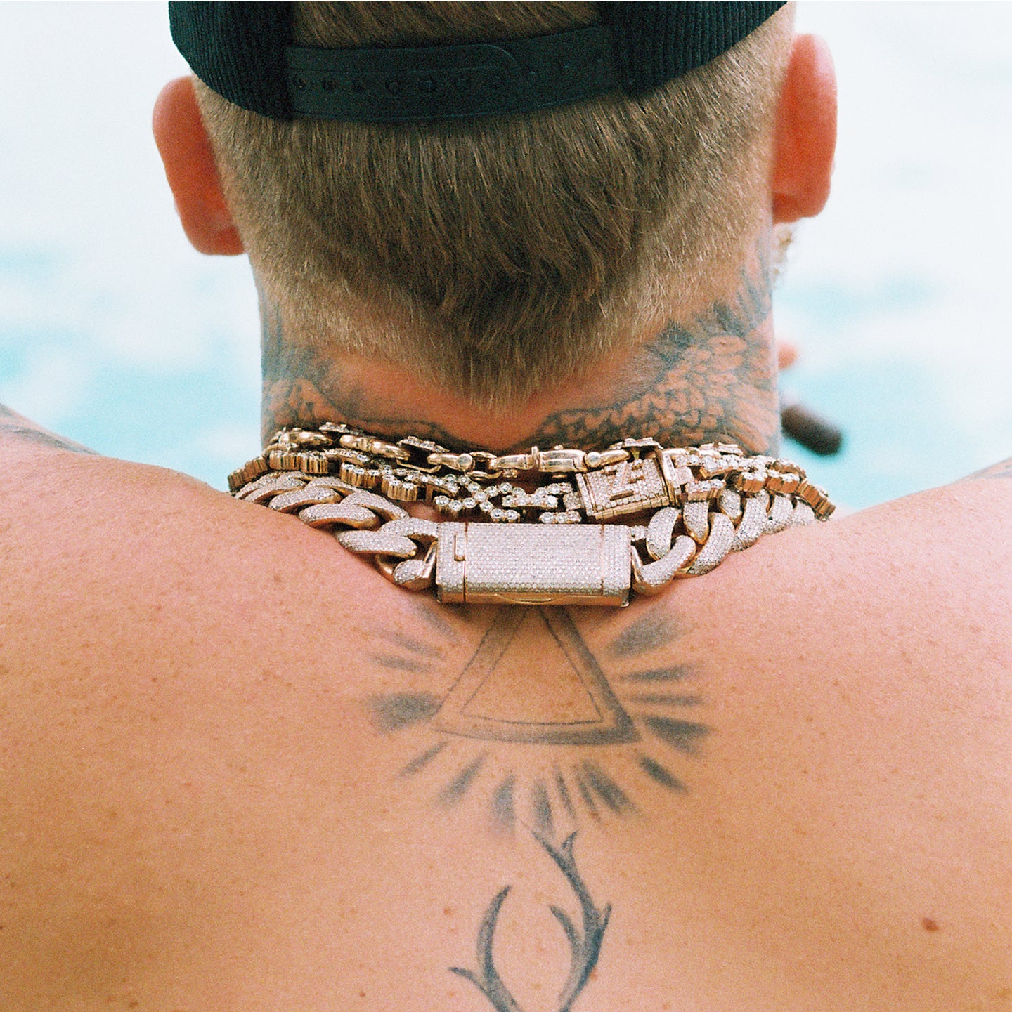 Person wearing multiple gold chains with tattoos on their neck and shoulder.