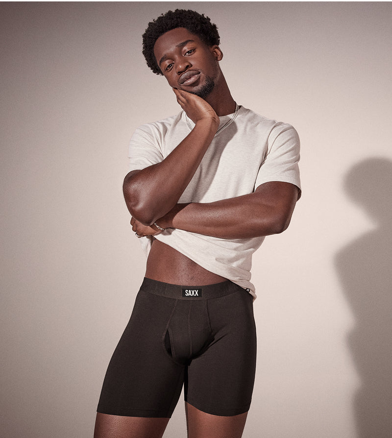 Man wearing a white t-shirt and black underwear with 'SAAX' branding against a plain background