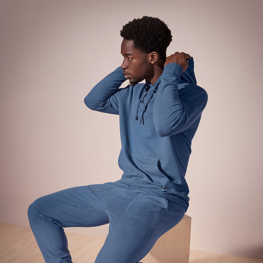 Man wearing a blue tracksuit sitting on a beige block against a beige background