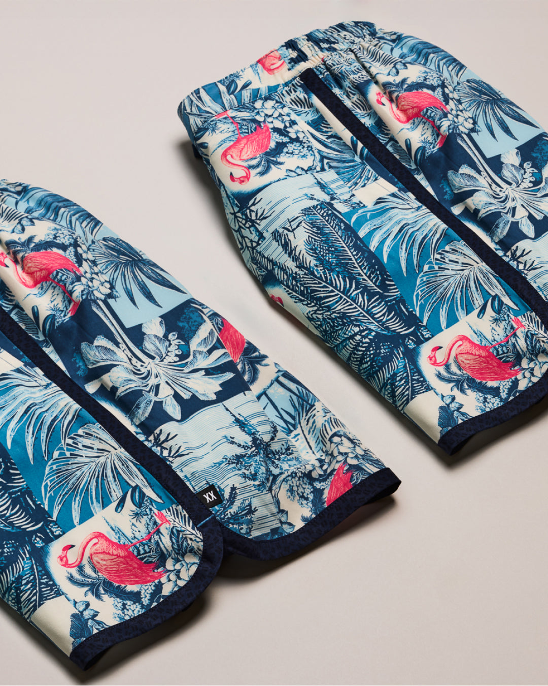 Two folded fabric items with flamingo and palm leaf pattern on a light gray background