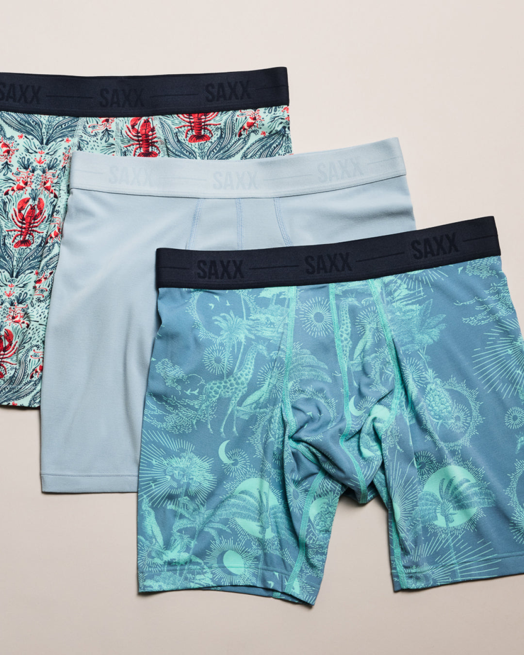 Three pairs of SAXX underwear with different designs on a beige background