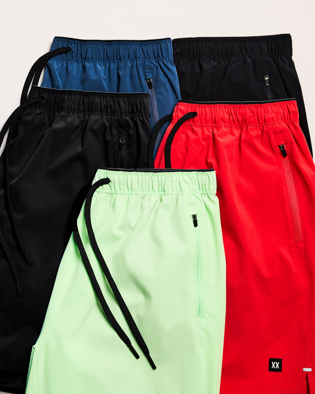 Four pairs of pants in black, blue, red, and green on a light gray background.