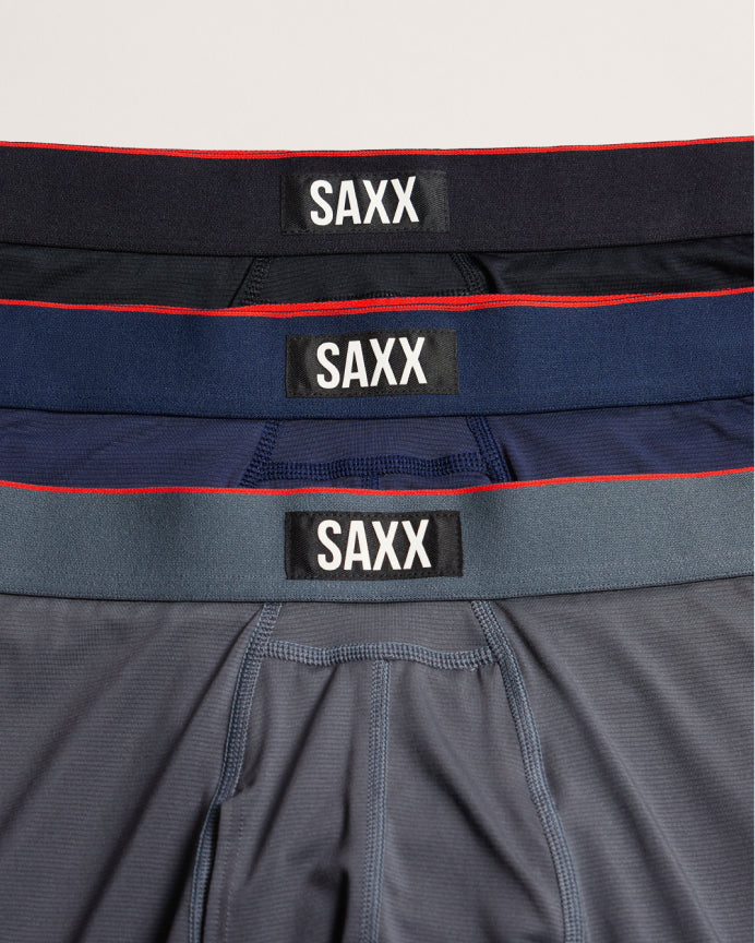 Three pairs of SAXX men's boxer briefs stacked vertically, showing the waistbands in black, navy, and slate blue with red piping accents.