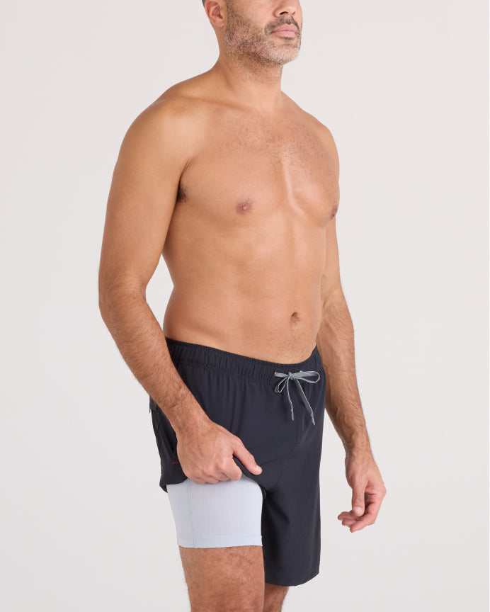 Man wearing black swim shorts with a white patch on a light gray background