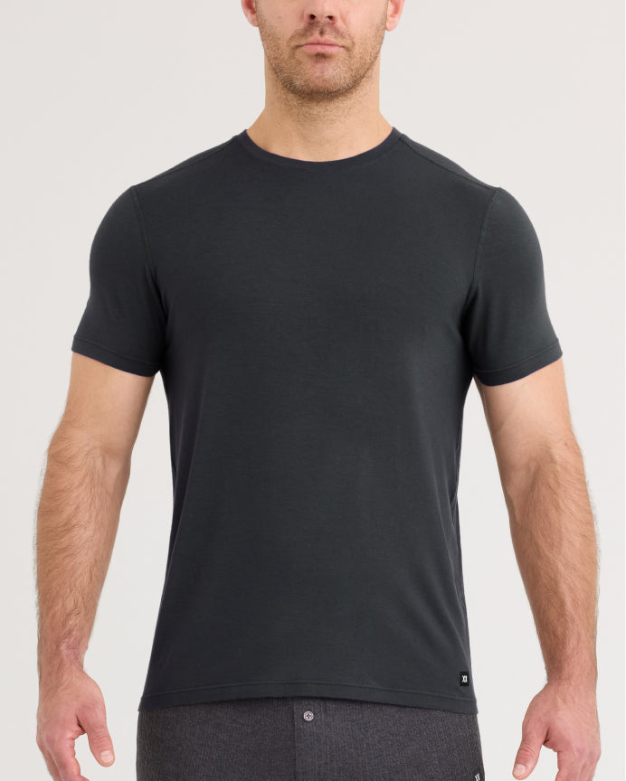 A man wearing a dark charcoal gray short-sleeve crewneck t-shirt, shown from the chest down against a light gray studio background.