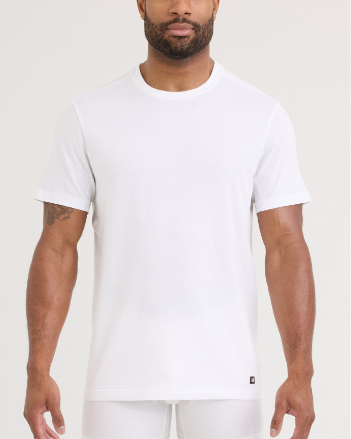 A man wearing a plain white short-sleeve crewneck t-shirt, shown from the chin down against a light beige studio background.