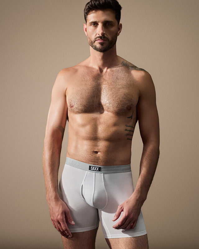 Man wearing white boxer briefs with 'SAXX' branding against a beige background