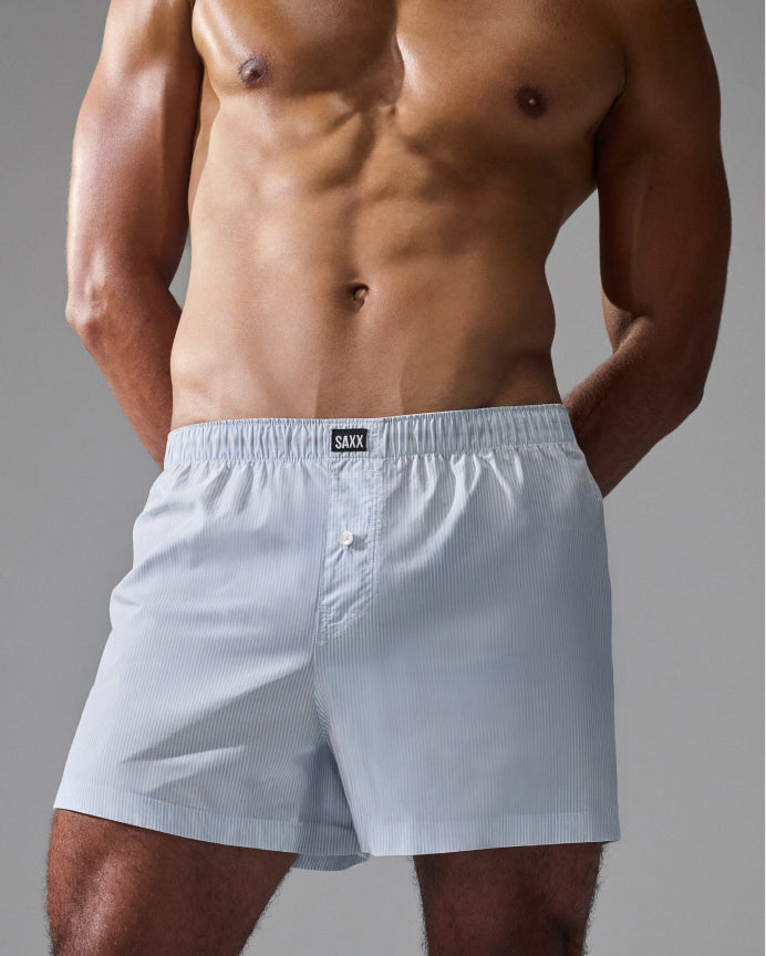 A close-up of a male model's lower torso wearing light blue pinstriped boxer briefs with a visible SALT brand label at the waistband, against a neutral gray studio background.