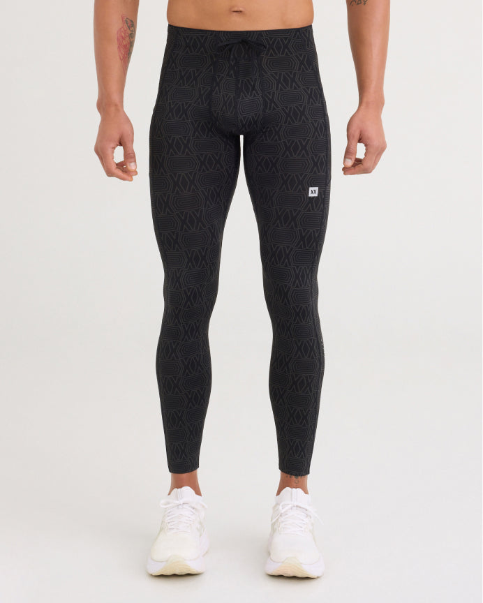 A model from the waist down wearing black high-waisted athletic leggings with a subtle tonal geometric pattern and white sneakers, set against a plain light gray studio background.