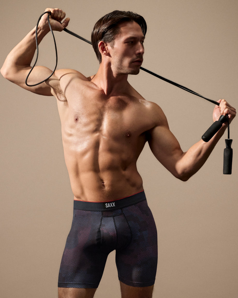 Man wearing SAXX underwear holding a jump rope against a beige background