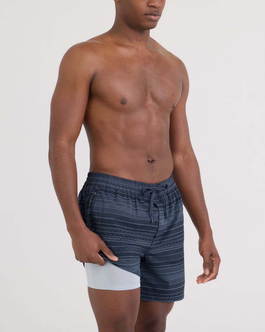 Man wearing SAXX navy striped swim shorts on a light gray background