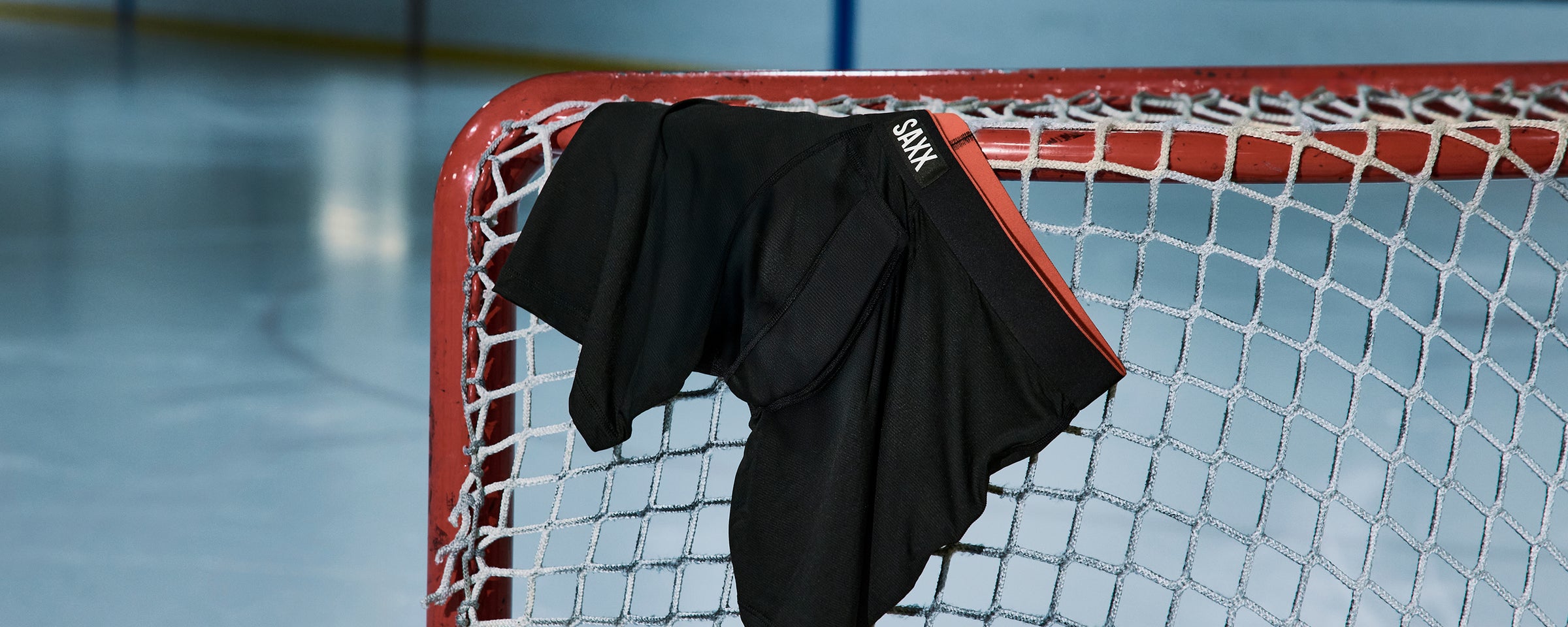 Black SAXX boxer briefs draped over a hockey net on an ice rink