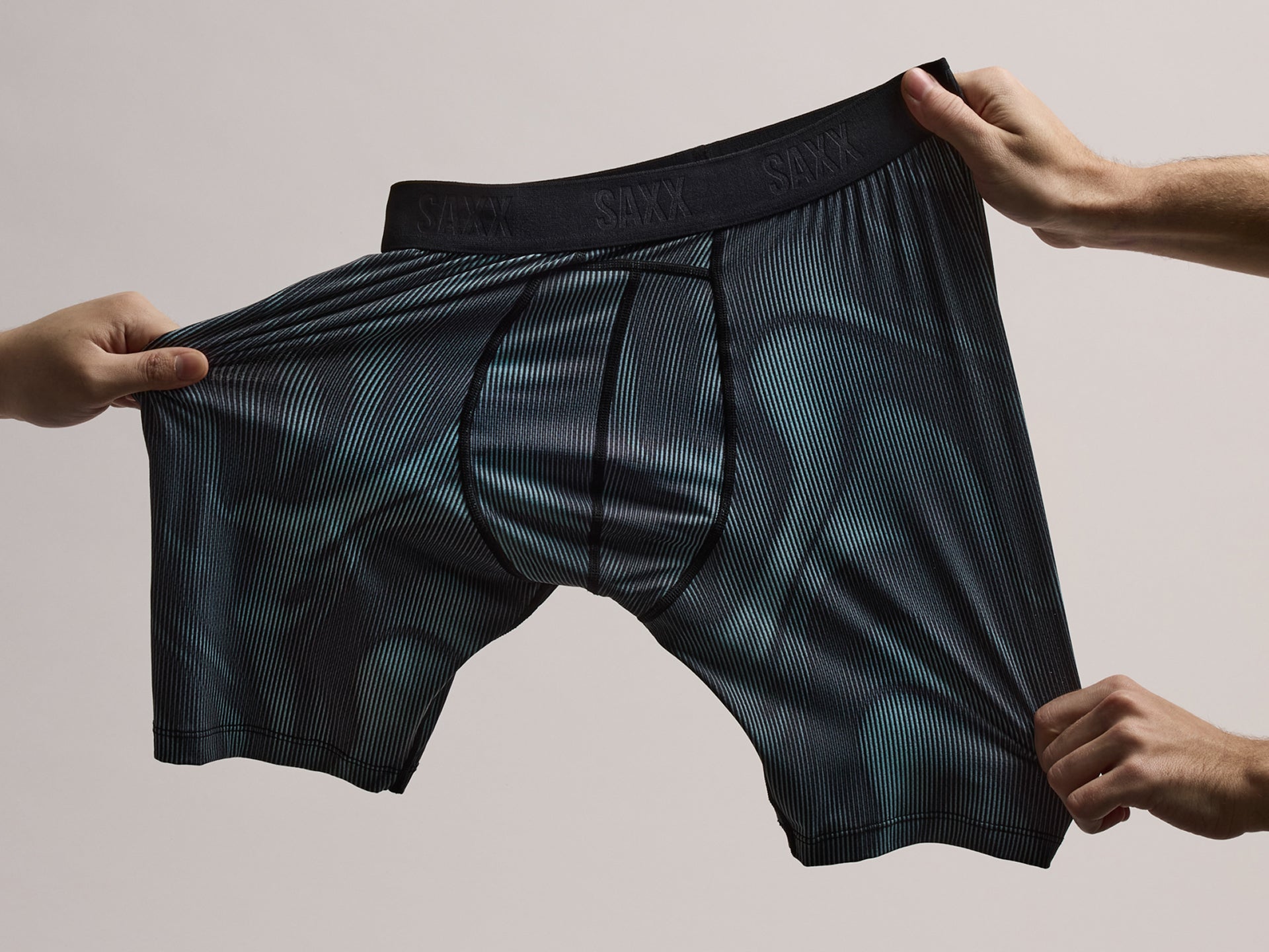 Black boxer briefs held open by two hands against a neutral background