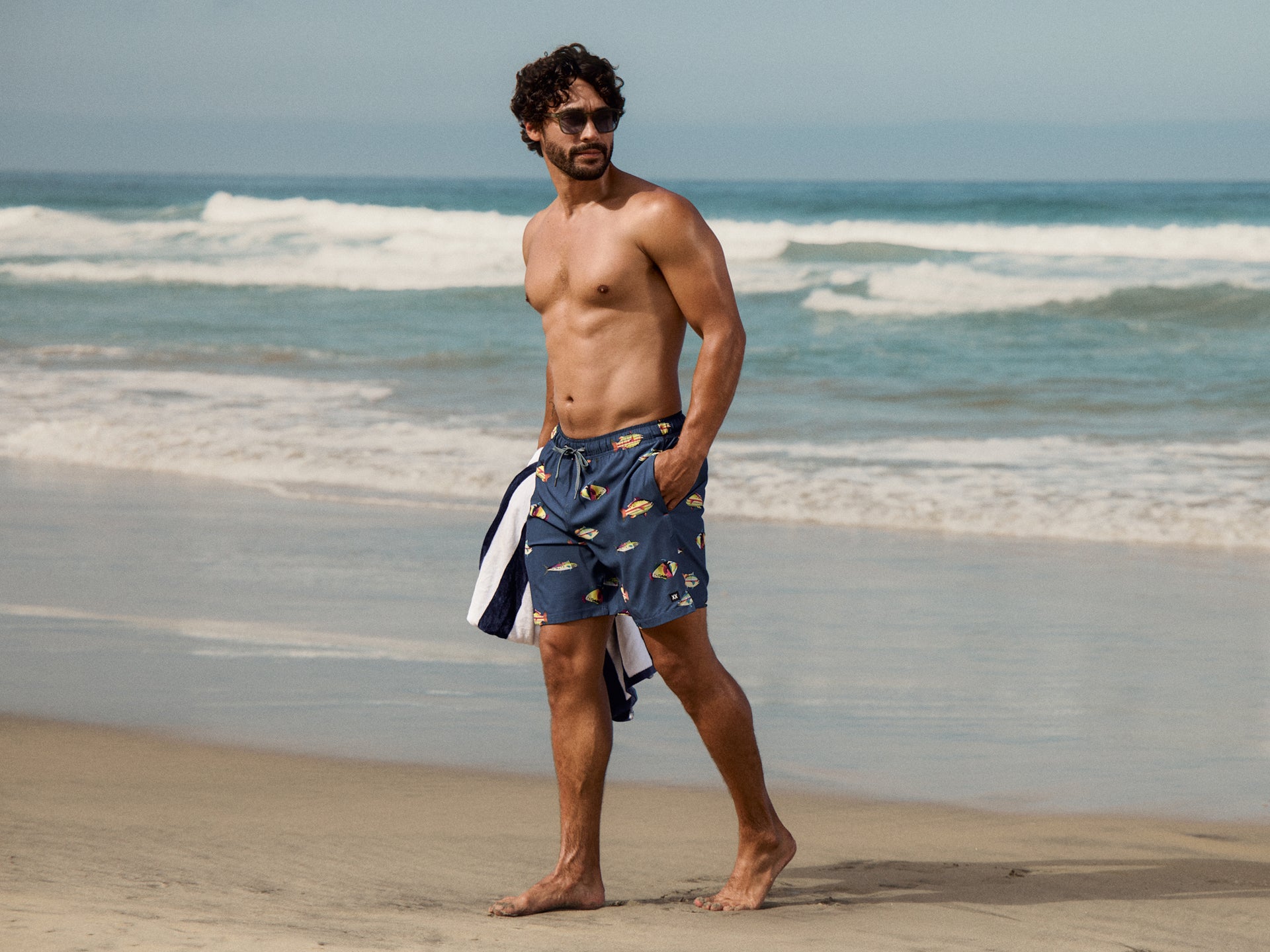 Man wearing blue swim trunks on a beach with ocean waves in the background