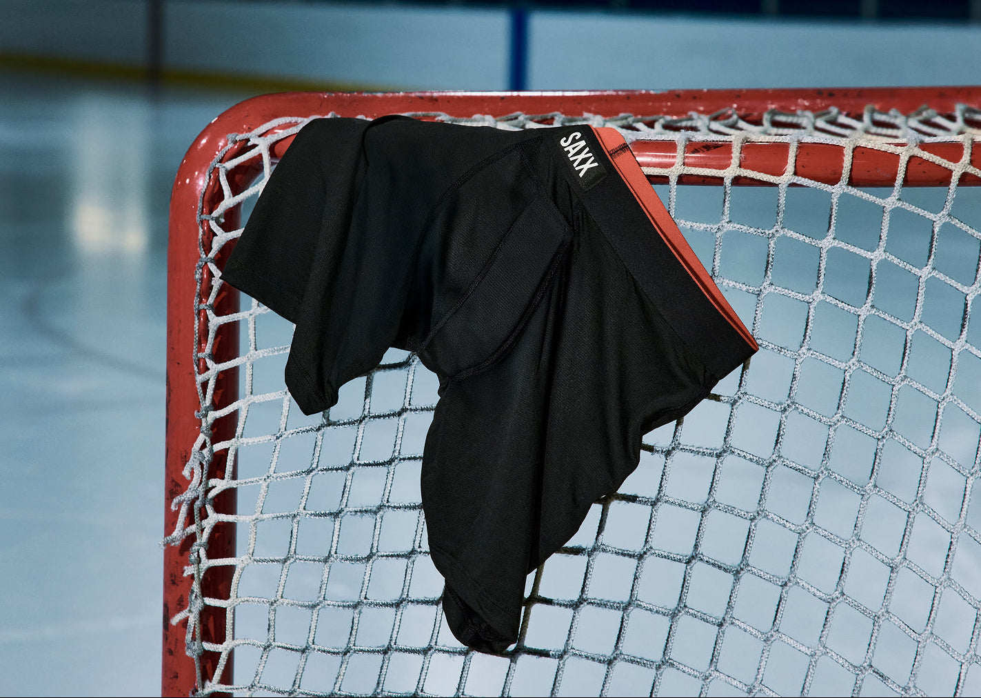 Black pair of Multi-Sport Mesh Boxer Briefs draped over a hockey net on an ice rink