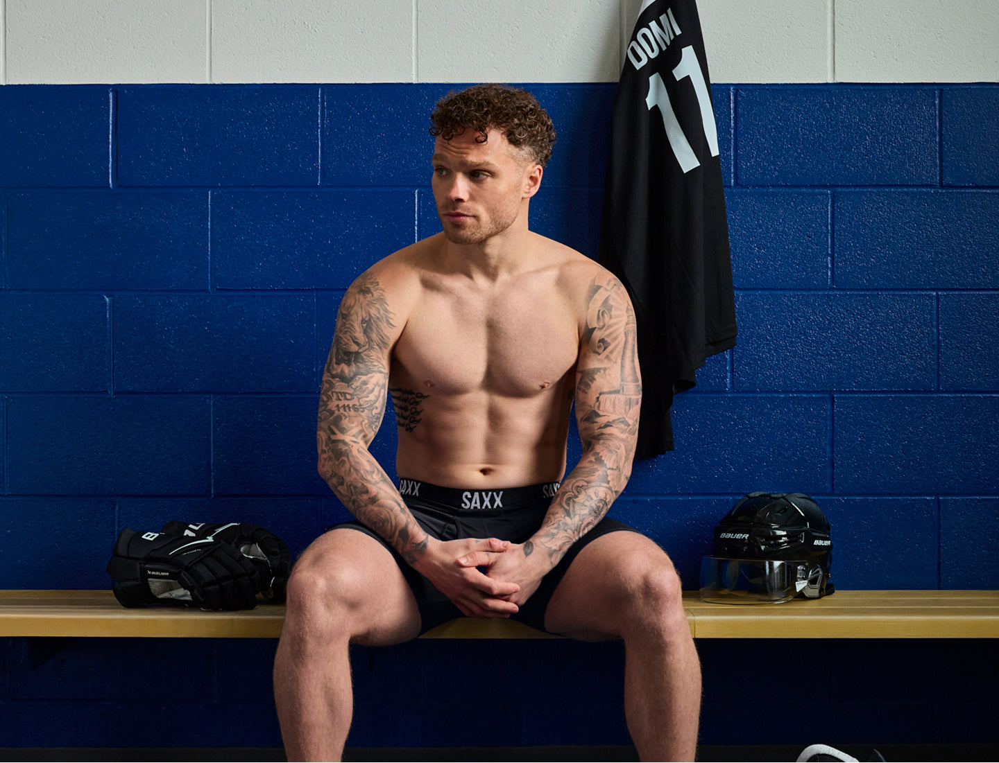 SAXX Gamechanger and Professional Hockey Player Max Domi, sitting on a bench in a locker room with blue walls and SAXX underwear.
